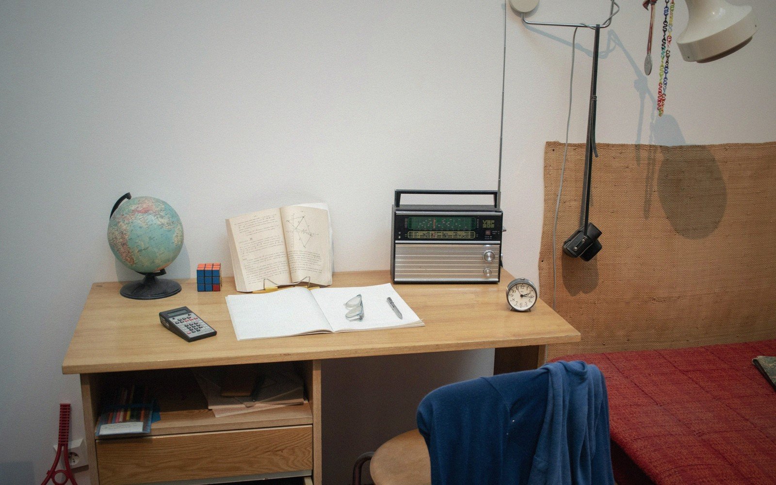 A wooden desk with a globe, radio, alarm clock and open notebook